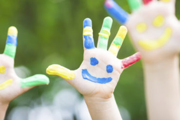 Children with painted red, blue smiling faces on their hands