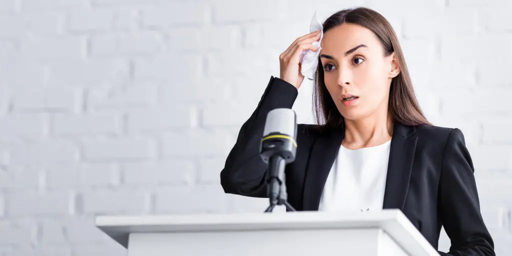 White brunette woman shows fear of public speaking at the podium in front of a microphone